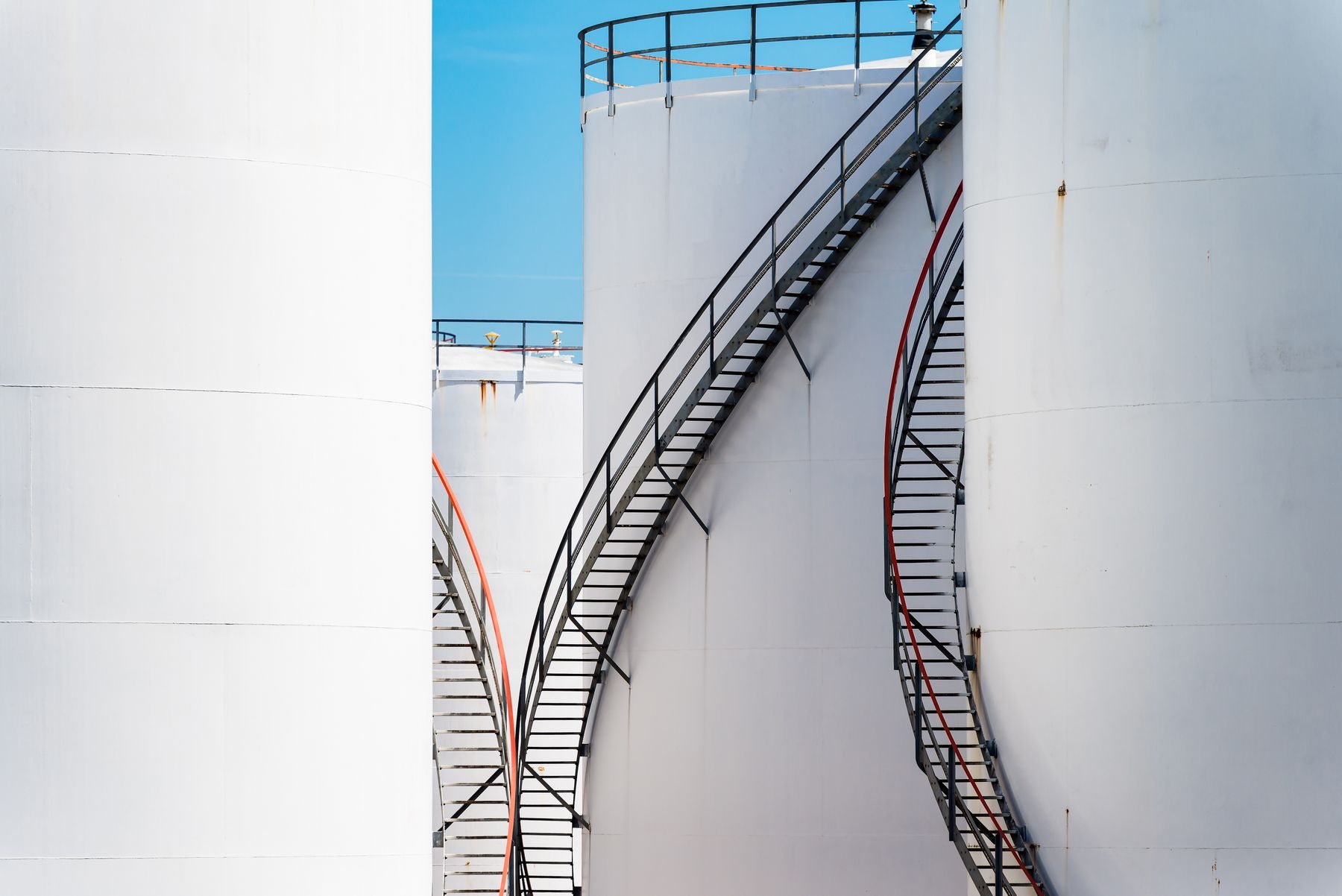 White industrial oil storage tanks under a clear blue sky